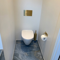 Flot udført toiletområde i nyt badeværelse, opbygget af erfaren murer i Aars med eksklusive gulvfliser og messingdetaljer.