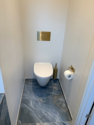 Flot udført toiletområde i nyt badeværelse, opbygget af erfaren murer i Aars med eksklusive gulvfliser og messingdetaljer.